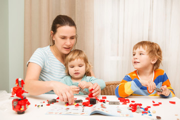 mother and children  playing with lots of colorful plastic blocks constructor and makes robot indoor.  The happy family spends time together at home.
Family and childhood concept. 
