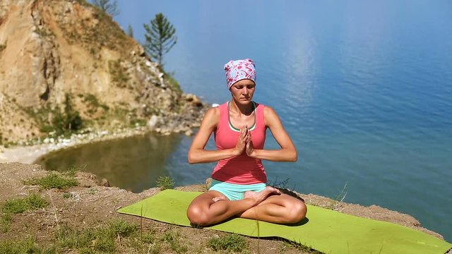Brunette professional yoga woman practices yoga moves outdoors near the giant blue lake baikal.
