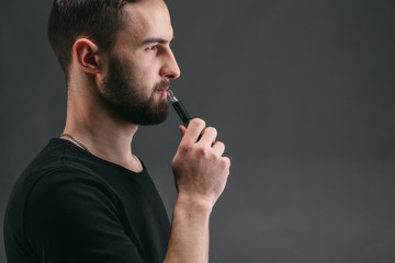 Young man vaping e-cigarette with smoke on black