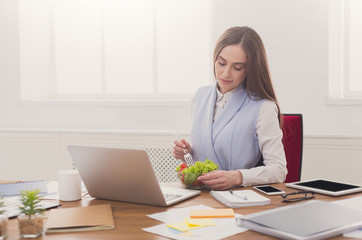 Young business woman eating salad at office
