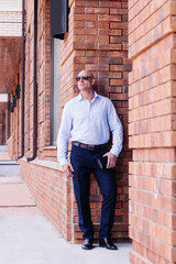 businessman full height outdoor staing at red brick building. shirt dark blue trousers, boots