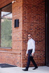bald strong businessman full height leaves the building red brick . shirt dark blue trousers, boots. spring, summer