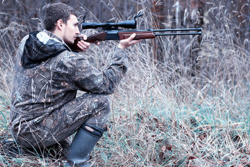 A man in camouflage and with a hunting rifle in a forest on a sp