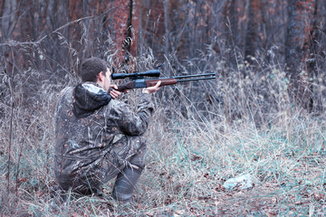 A man in camouflage and with a hunting rifle in a forest on a sp