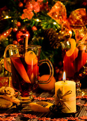 Christmas and New Year mulled wine with cinnamon, cardamom and anise on a background of spruce branches, snowflakes and burning candles, dark toned image, selective focus