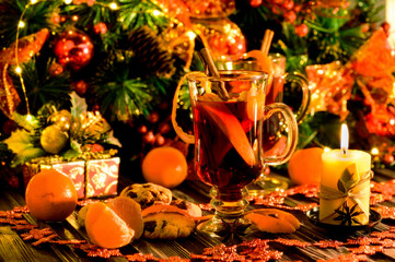 Fototapeta na wymiar Christmas and New Year mulled wine with cinnamon, cardamom and anise on a background of spruce branches, snowflakes and burning candles, dark toned image, selective focus