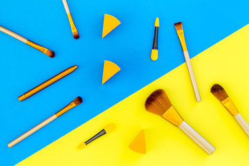 Set of brushes for makeup and eyeshadow applicator on blue and yellow background top view