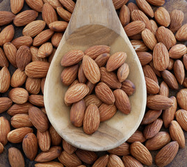 Almonds in wooden spoon on almonds background.