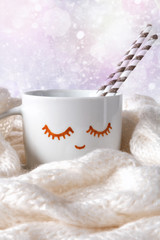 Obraz na płótnie Canvas White cup with cocoa and marshmallow with painted eyes in a cozy scarf on a light background with copy space