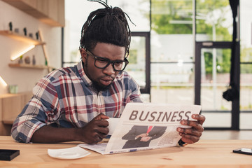 focused african american man drinking coffee and reading business newspaper