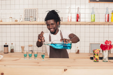 african american bartender pouring blue drink into shot glasses at bar counter