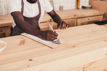 cropped view of african american barista taking order at bar counter
