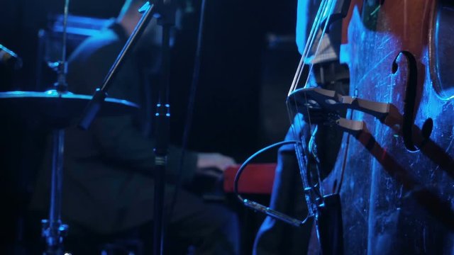Musician playing contrabass with pianist on background close-up. Man artist play wooden double bass on stage dark background