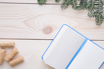 Christmas light wooden background with fir tree branches a blank notebbok in a blue cover and cookies. Close up. Copyspace