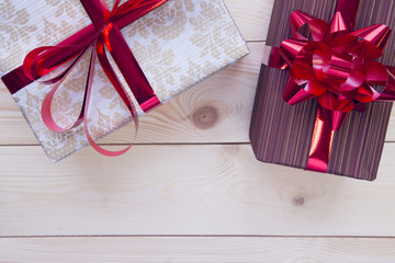 A white patterned giftbox,a purple striped gift box. Red shiny ribbons on the gift boxes. Light wooden background. Top view. Close up. Copyspace