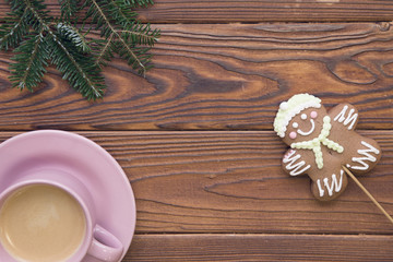Christmas rustic wooden background with fir tree branches, pink coffee cup with a hot cappuchino and a gingerbread man. Top view. Close up. Copyspace