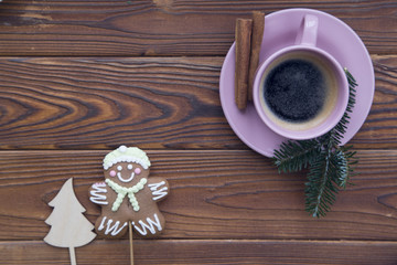 Christmas rustic wooden background with fir tree branches. A hot espresso in a pink porcelian cup with sticks of cinnamon on a saucer, a gingerbread man and snowman. Top view. Close up. Copyspace