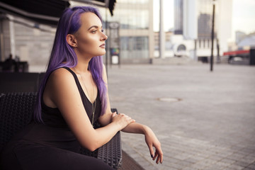 Beautiful brunette woman with colored (purple violet blue) hair in dark black slim dress outdoor in...