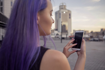 Fototapeta na wymiar Beautiful brunette woman with colored (purple violet blue) hair in dark black slim dress outdoor in the european city, smiling, typing, playing, make photo on her phone