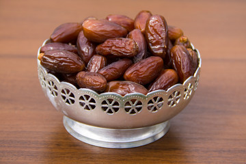 Dates fruit on a silver bowl on wooden table. The Muslim feast of the holy month of Ramadan Kareem