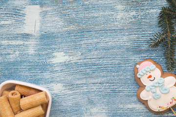 A blue wooden Christmas background with fir tree branches, a gingerbread snowman and a bowl of cookies. Top view. Close up. Copyspace