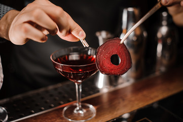 Barman decorating a red cocktail drink with a slice of a beet