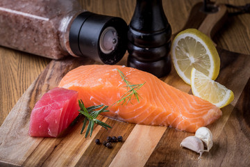 Salmon and Tuna raw. Red fish steak with herbs and lemon on wooden plate.