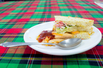 vegetables sandwiches serve with fried potato good food and healthy for diet and control weight with the tomatoes sauce on the white disc and the Stainless spoon on the Scottish chintz