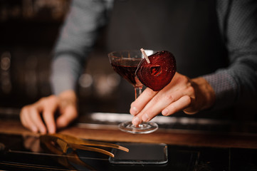 Bartender holding a glass of red decorated alcoholic drink