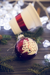 A festive composition with white fairy lights, a paper cup with a red ribbon unfocused and a red Christmas tree ball on a dark wooden background. Close up. Copyspace
