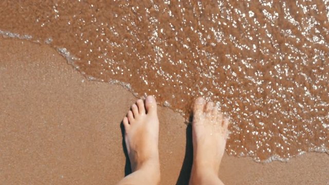 Mediterranean Sea waves washing woman's feet at a sandy beach