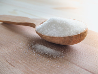 White sugar and wooden spoon on a wooden table.