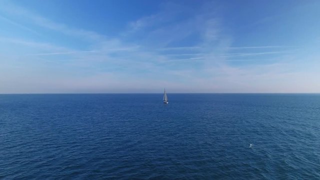 Beautiful and inspiring aerial shot from drone footage of professional yacht or sailboat with mainsail and spinnaker up, cruising in open empty blue waters of sea or ocean on clear summer day