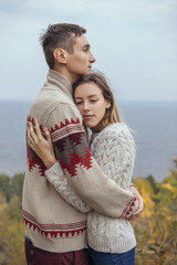 Happy thoughtful couple standing on a cliff near sea hugging each other in cold foggy cloudy autumn weather. Copy space