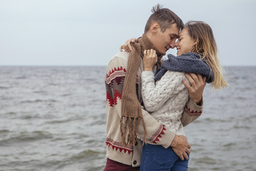 Happy thoughtful couple standing on a rock beach near sea hugging each other in cold foggy cloudy autumn weather. Copy space