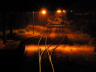 leerer Güterbahnhof mit abgestelltem Waggon und orangener Straßenbeleuchtung bei Nacht	