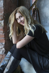 Cute blonde caucasian woman sitting in loft grunge trendy minimalistic interior, smiling cheerfully