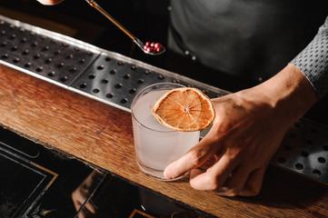 Barman decorating a glass filled with a murky alcoholic drink