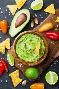 Avocado guacamole with  ingredients pepper, lime and nachos on black table top view. Traditional mexican food.