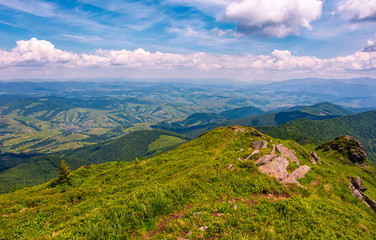 grassy slope with huge boulders. view to rural valley with forested hills. fine summer day with good weather under the blue sky with some clouds