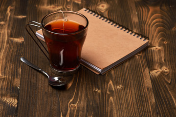 Tea and notebook on wooden background.