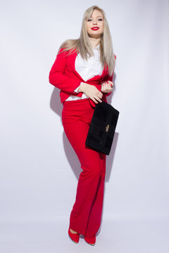 Portrait of a beautiful young blond woman with long hair in a red suit. She holds a big black clutch in her hands.