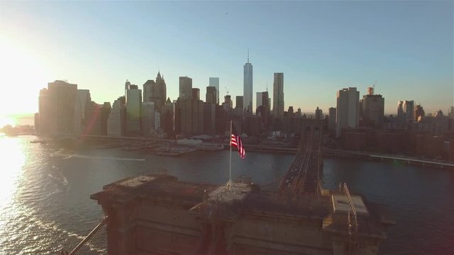 Aerial view of Brooklyn bridge on a sunny day. Camera crossing the bridge moving near a flapping American flag in the direction of Manhattan, Manhattan panorama.