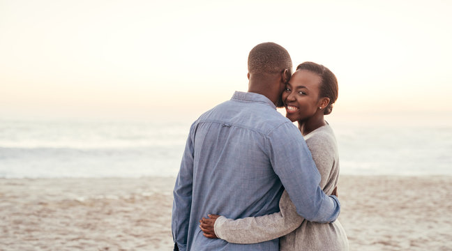 African woman embracing her boyfriend on a beach at sunset