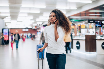 Young woman at the airport with trolley bag, talking on the phone.