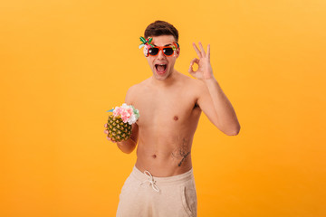 Fototapeta premium Happy naked man in shorts and unusual sunglasses holding cocktail