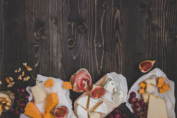Various types of cheese with fruits and snacks on the wooden dark table with copy space
