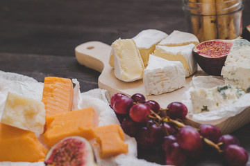 Various types of cheese with fruits and nuts on the wooden dark table. Selective focus