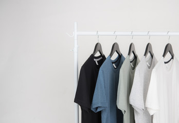 Black,blue, grey and white t-shirts on hangers on gray background