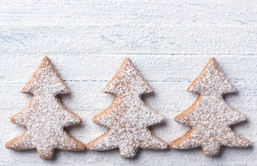 Oatmeal gingerbread cookies in the shape of Christmas tree sprinkled with powdered sugar on a light blue background, top view, free space